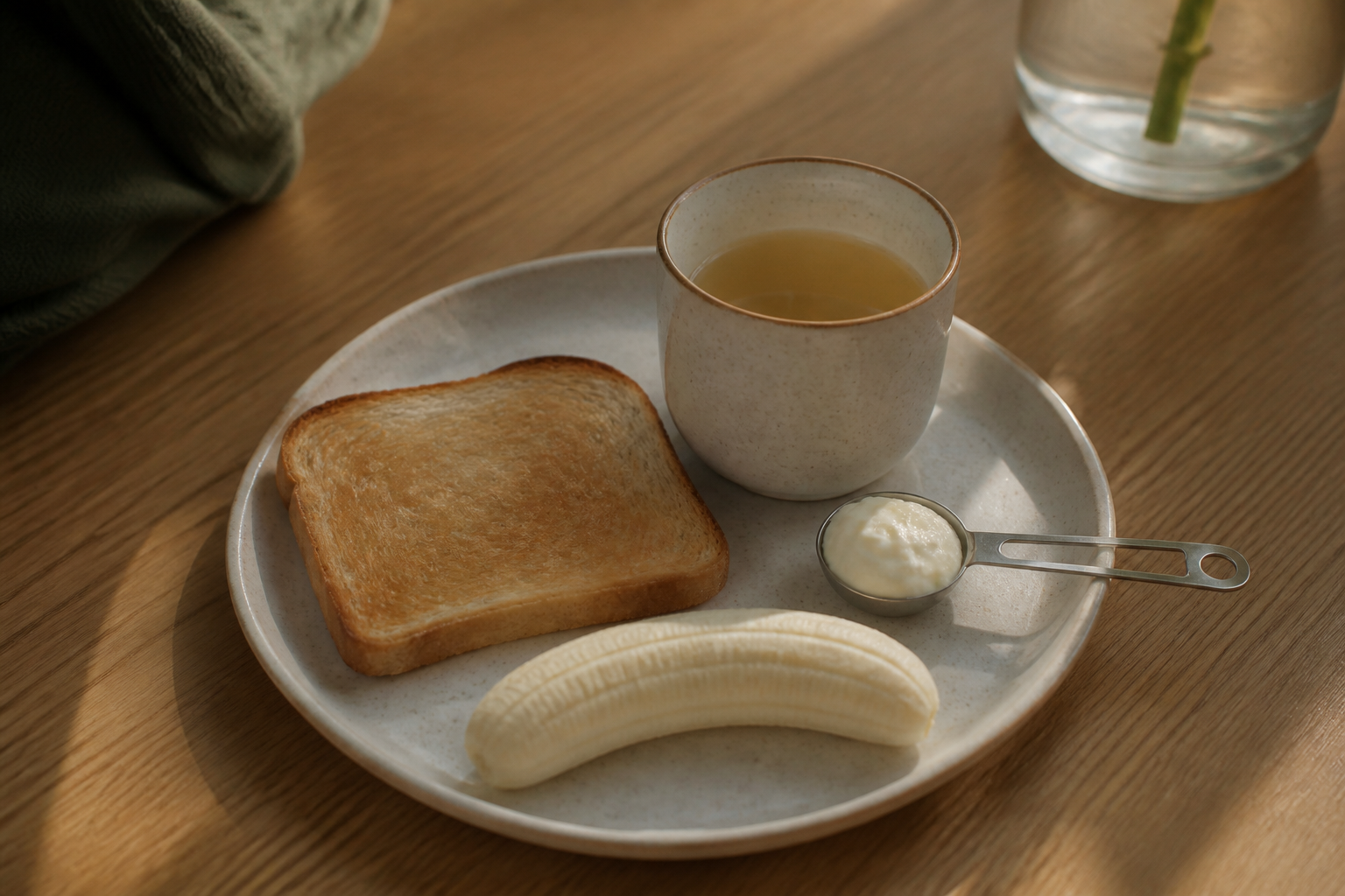 Small bland meal plate with toast, banana, yogurt and ginger tea to illustrate anti-nausea foods.